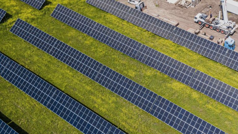 Vista aérea de una planta fotovoltaica con una grúa y casetas de obra entre las filas de módulos