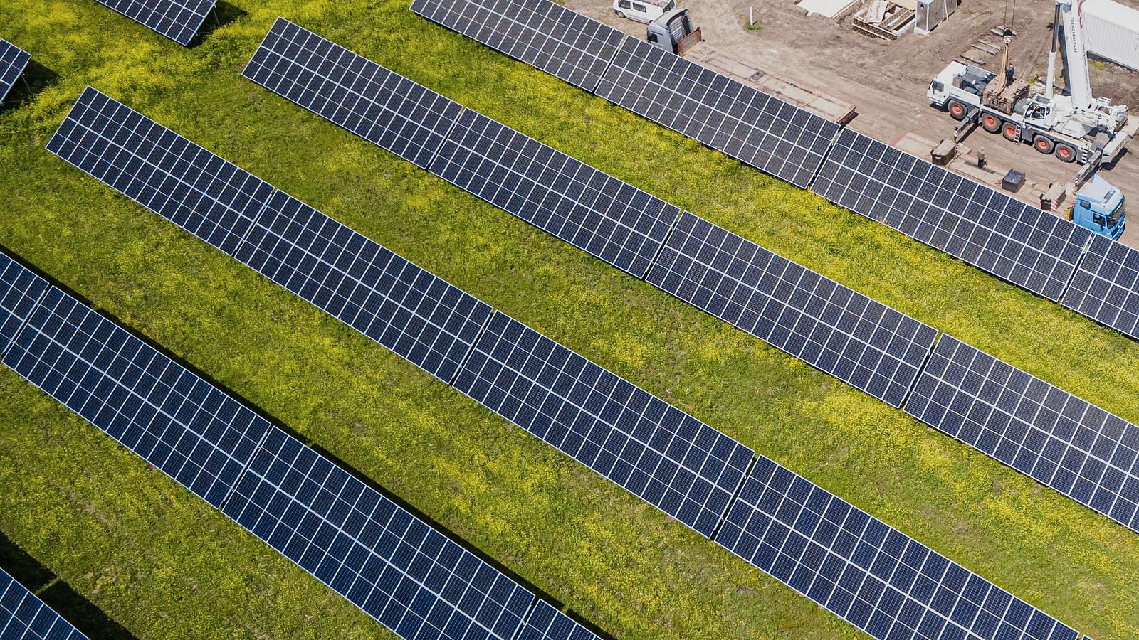 Vista aérea de las filas de módulos de una planta fotovoltaica, con una grúa trabajando al fondo