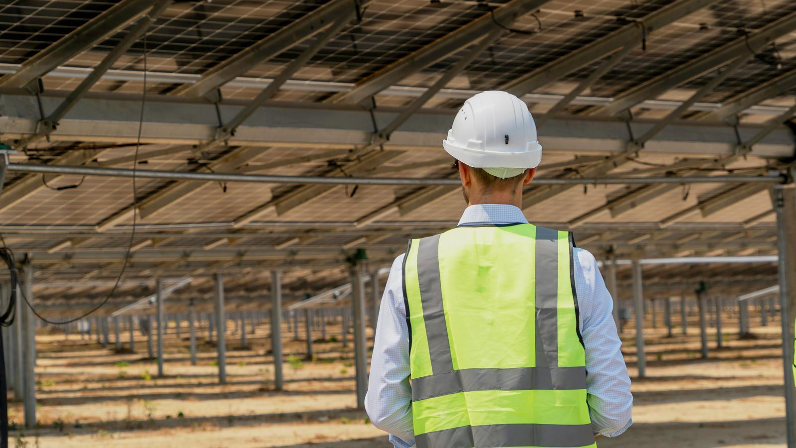 Técnico con casco y chaleco recorriendo una planta fotovoltaica de seguidores